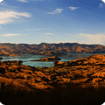 Scenic landscape view of rolling hills and a tranquil lake under a clear blue sky, showcasing natural beauty and outdoor tranquility.