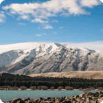 Snow-capped mountains against a clear blue sky with a serene lake in the foreground, showcasing the natural beauty of a tranquil landscape.