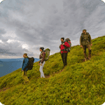 Group of hikers exploring a lush green hillside under a cloudy sky, showcasing outdoor adventure and teamwork in nature.