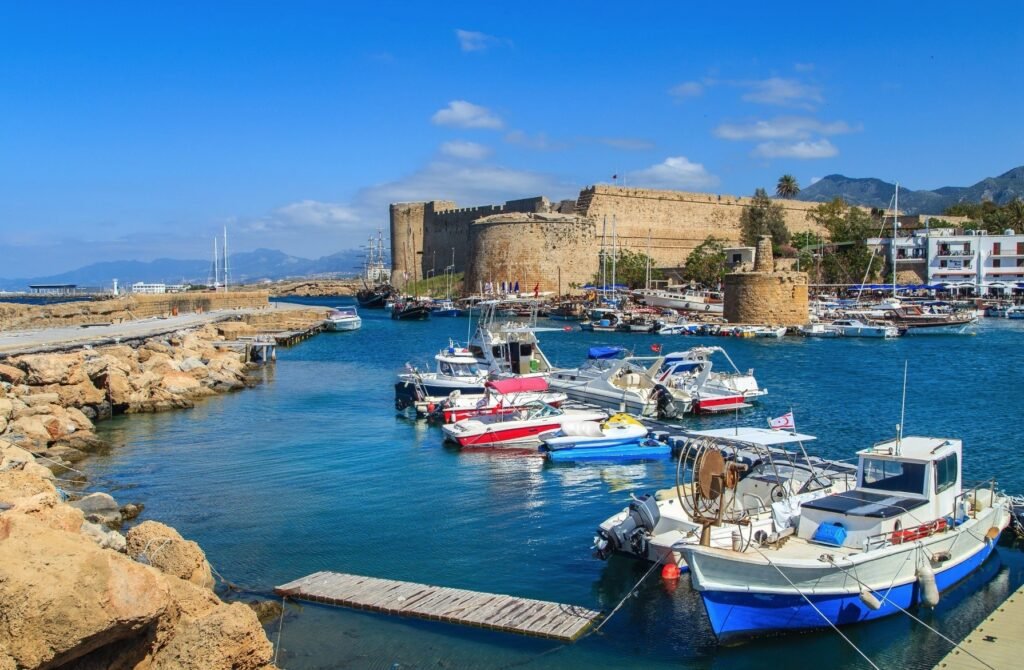 Scenic view of a harbor in Cyprus featuring moored boats and a historic castle in the background under a clear blue sky.
