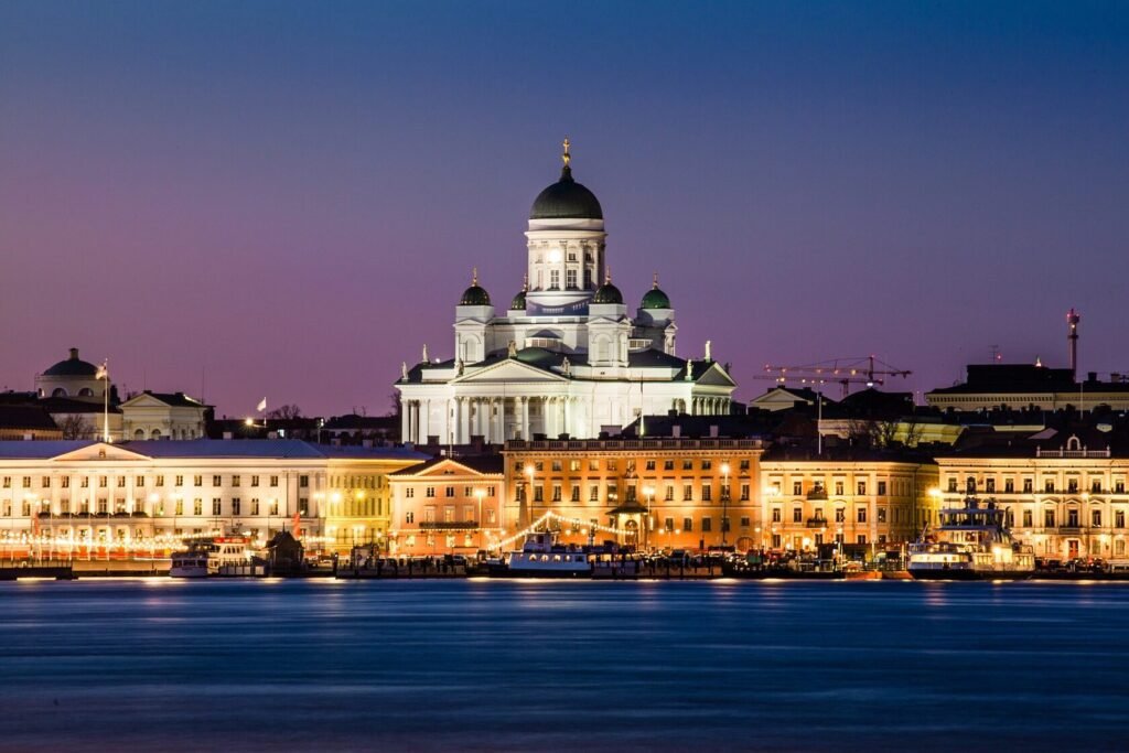 Helsinki Cathedral illuminated at dusk, overlooking the waterfront with historic buildings in the foreground.