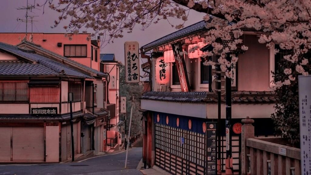Charming street view in Japan during twilight, featuring traditional wooden buildings, illuminated signs, and cherry blossom trees in bloom.