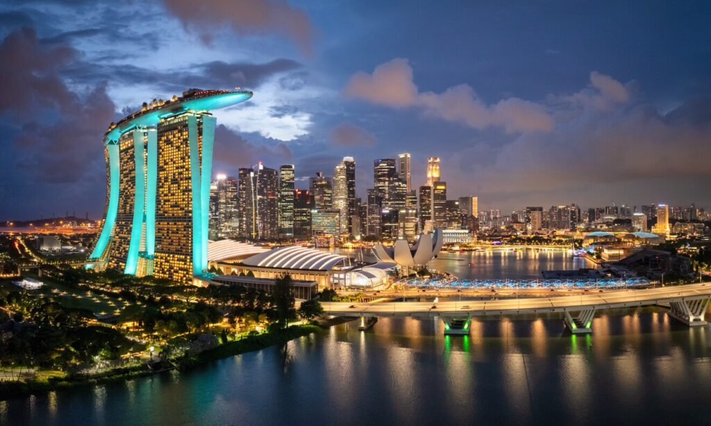 Singapore skyline at night featuring the iconic Marina Bay Sands, illuminated buildings, and a serene waterfront reflecting city lights.