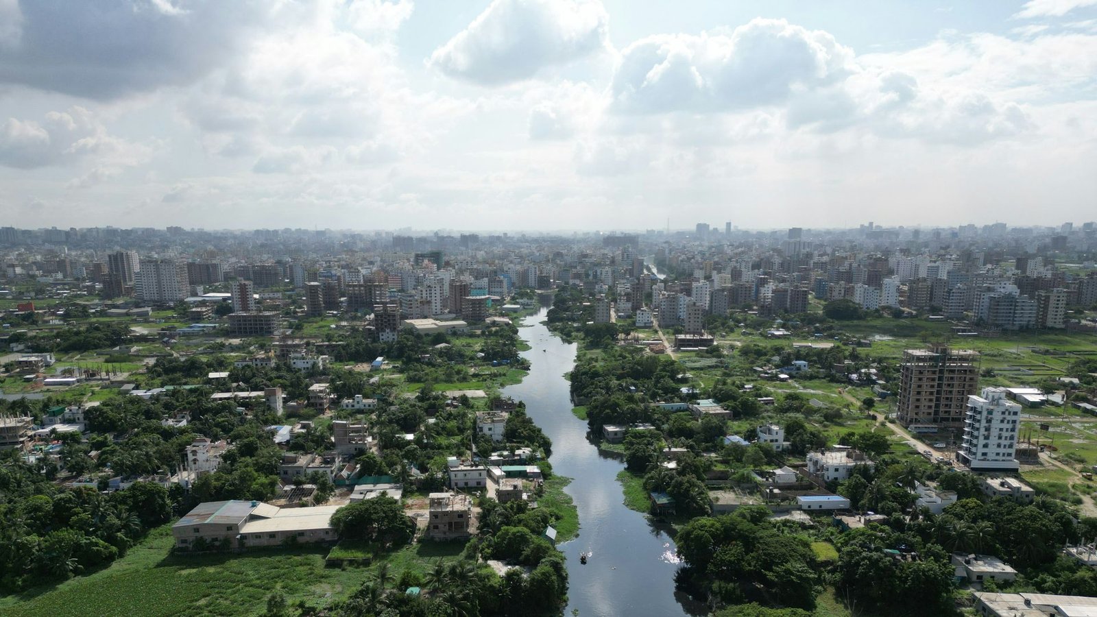 Aerial view of a cityscape featuring a winding river surrounded by green landscapes and urban development under a partly cloudy sky.