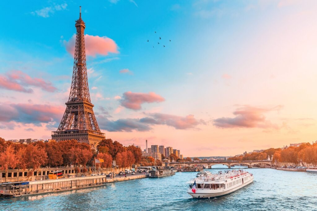 Eiffel Tower at sunset, with a scenic view of the Seine River and a boat cruising along the water, showcasing Paris's iconic landscape.