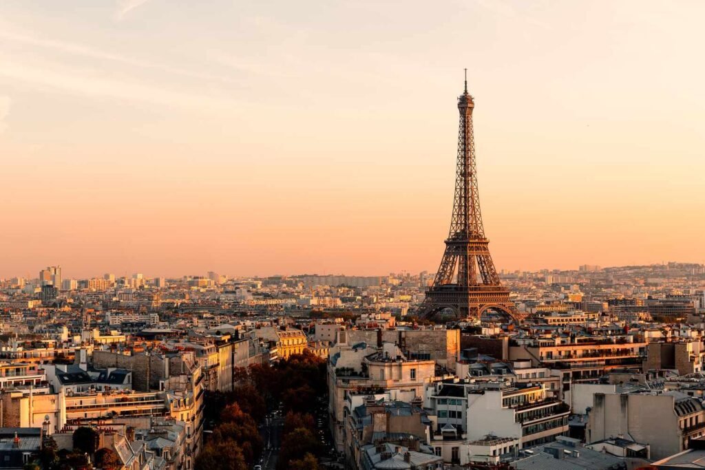 Panoramic view of Paris at sunset featuring the iconic Eiffel Tower surrounded by the city's skyline and warm evening light.