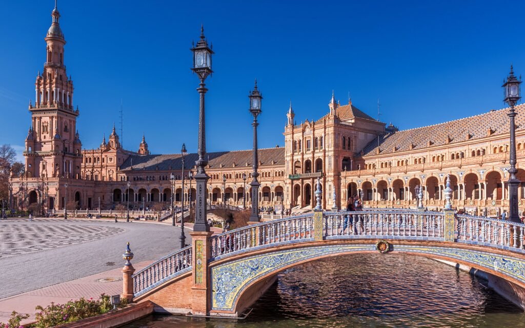 Beautiful view of Plaza de España in Seville, Spain, featuring an ornate bridge and stunning architectural details under a clear blue sky.