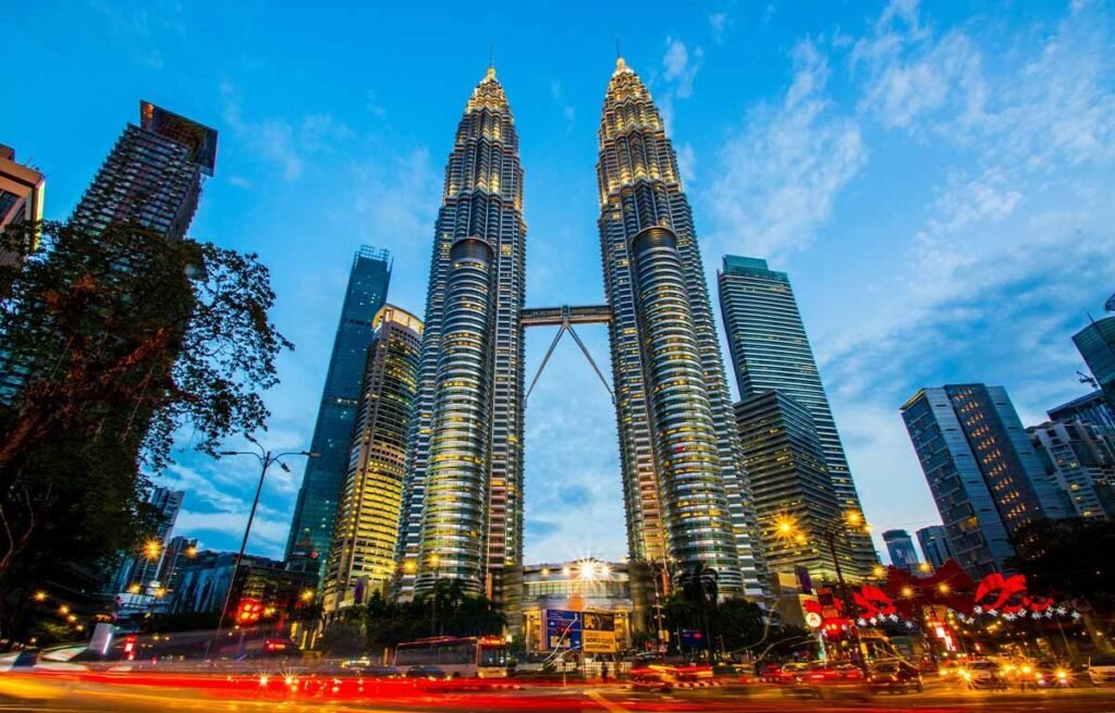 Petronas Twin Towers in Kuala Lumpur, Malaysia, illuminated at dusk with a vibrant city skyline and traffic in the foreground.
