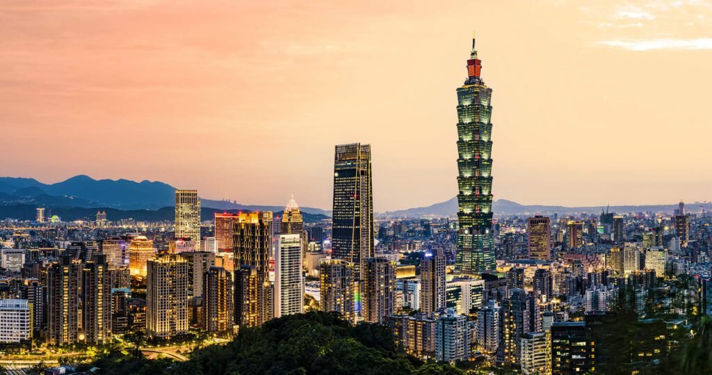 Taipei skyline at sunset featuring Taipei 101, a famous skyscraper, surrounded by urban buildings and mountains in the background.