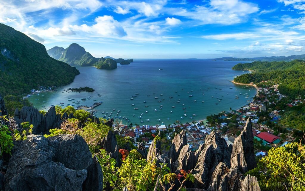 Breathtaking panoramic view of a coastal landscape featuring rocky cliffs, a serene bay filled with boats, and lush greenery under a clear blue sky. Ideal for travel and nature enthusiasts.