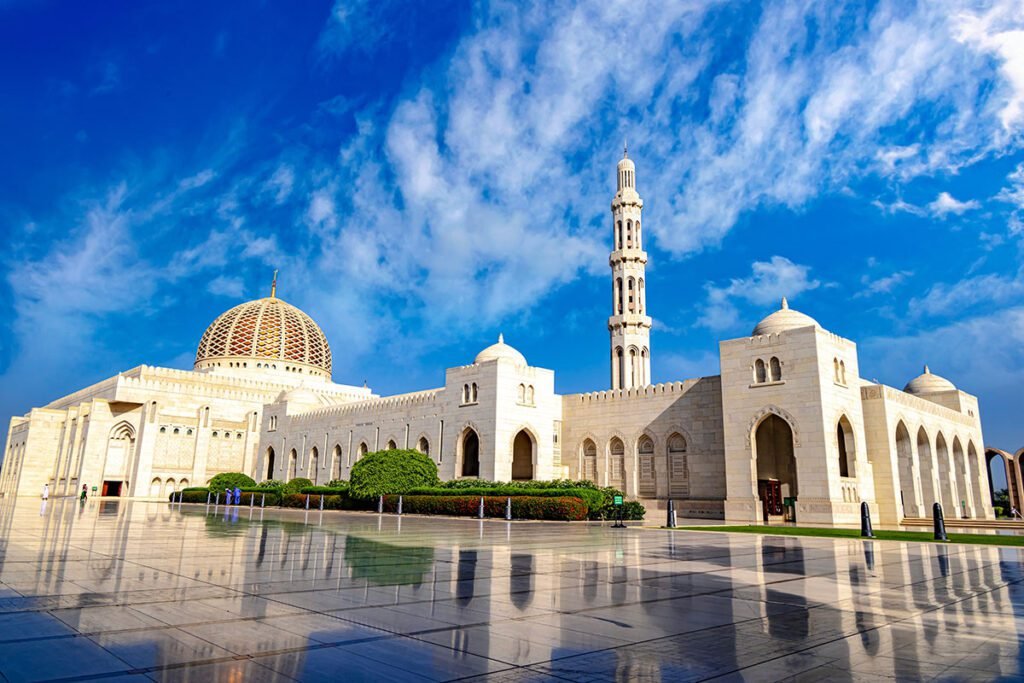 Sultan Qaboos Grand Mosque in Muscat, Oman, showcasing its stunning architecture, intricate details, and beautiful landscape under a clear blue sky.