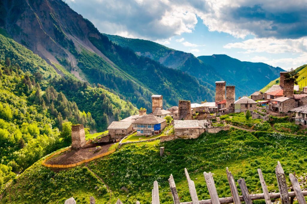 Scenic view of traditional Svan towers and village nestled in lush green mountains of Georgia, under a dramatic sky.