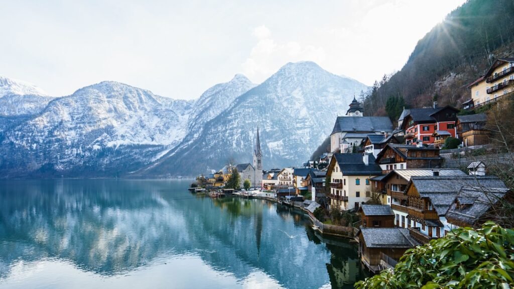 Scenic view of Hallstatt, Austria, featuring traditional alpine architecture along a serene lake, surrounded by snow-capped mountains and a clear blue sky. Ideal destination for nature lovers and photographers.