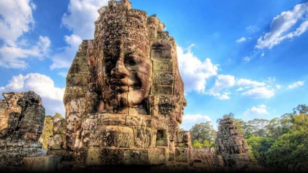 Stone faces of Bayon Temple in Angkor Thom, Cambodia, against a blue sky, showcasing intricate carvings and historical significance.