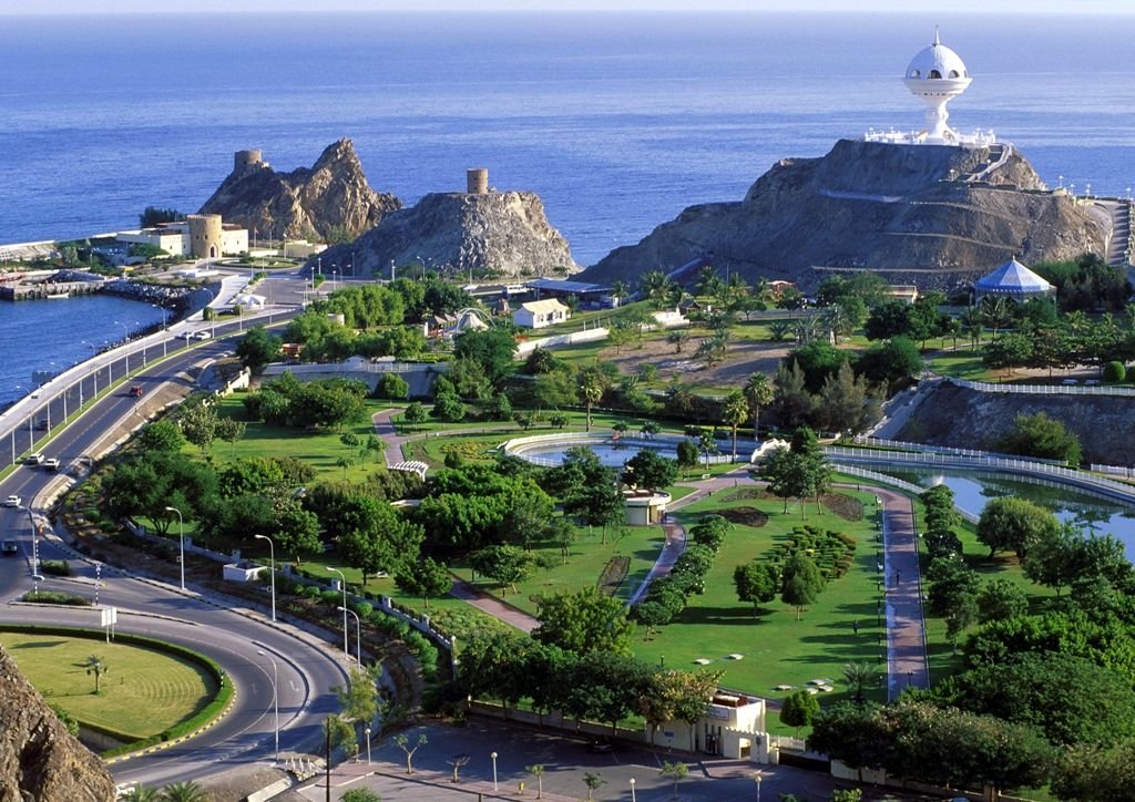 Aerial view of a coastal landscape featuring lush greenery, winding roads, and rocky cliffs overlooking the ocean, with a communication tower on the hill in the background.