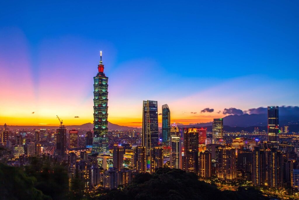 Taipei skyline at sunset featuring Taipei 101, with vibrant colors illuminating the cityscape and surrounding mountains.