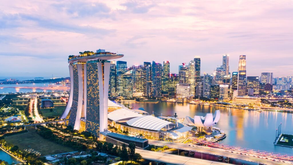 Aerial view of Singapore's skyline at sunset, featuring the iconic Marina Bay Sands hotel and the ArtScience Museum, surrounded by modern skyscrapers and reflecting waters.