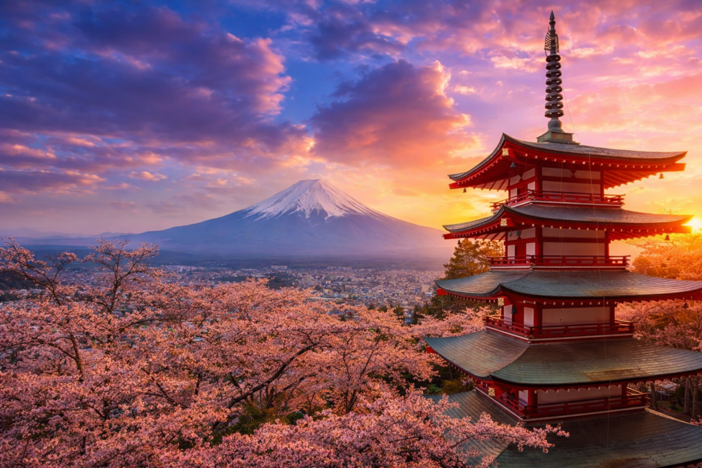 Cherry blossoms in full bloom surround a traditional Japanese pagoda, with Mount Fuji in the background under a vibrant sunset sky. This picturesque scene captures the beauty of Japan's natural and architectural landscapes.