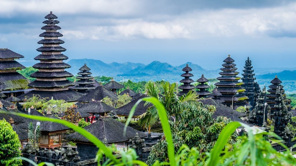 Scenic view of traditional Balinese temples surrounded by lush greenery and mountains under a cloudy sky in Bali, Indonesia.