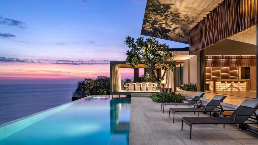 Modern luxury villa with an infinity pool overlooking a scenic sunset, featuring elegant outdoor seating and lush landscaping. Ideal for vacation rentals and upscale getaways.