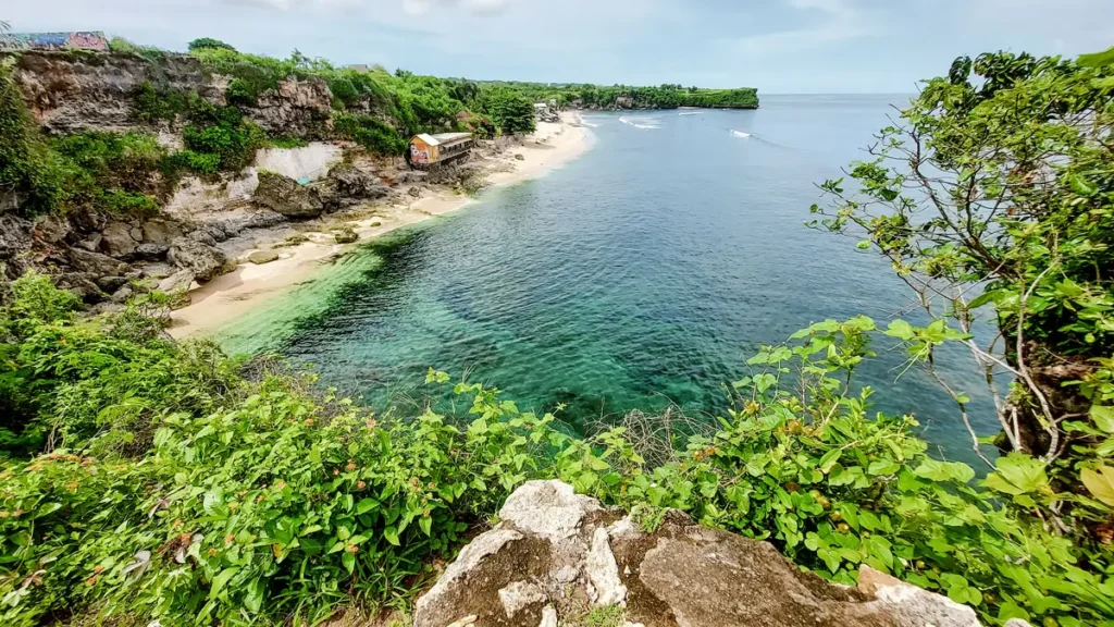 Scenic view of a tranquil beach with clear turquoise waters and lush greenery, showcasing rocky cliffs and a sandy shoreline. Ideal for nature lovers and beach enthusiasts.