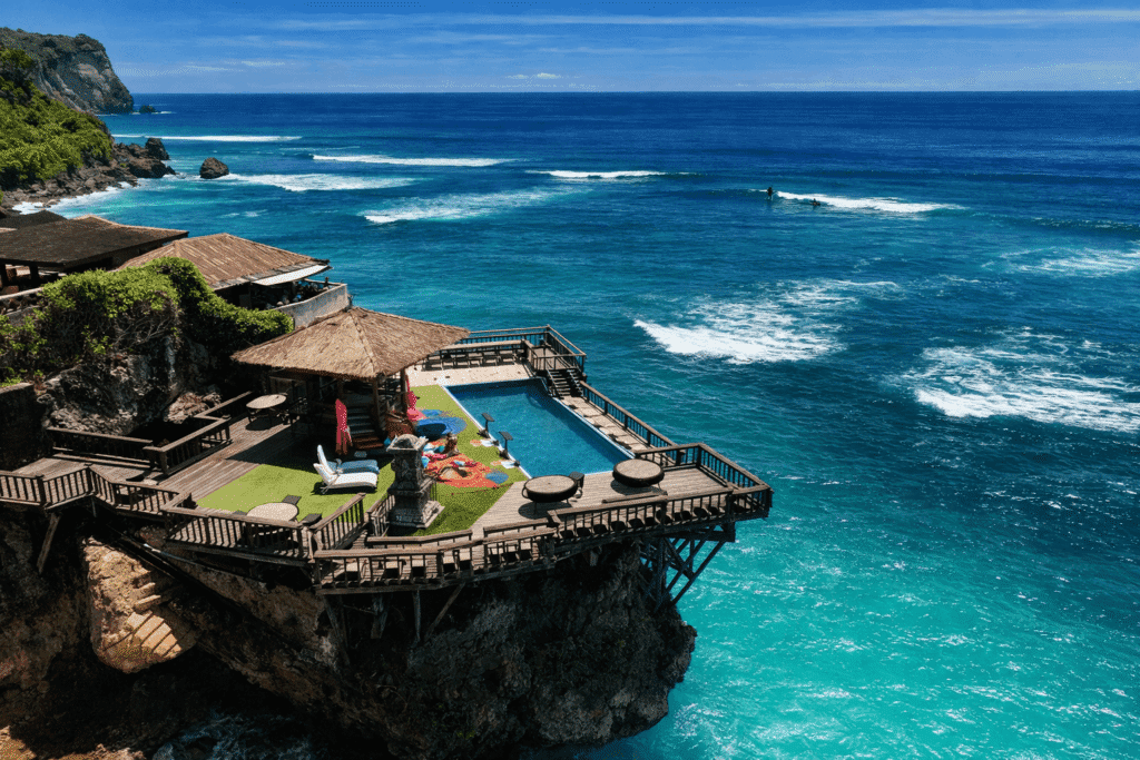 Stunning coastal villa with a private infinity pool overlooking the turquoise ocean, surrounded by lush greenery and rocky cliffs, perfect for a tropical getaway.