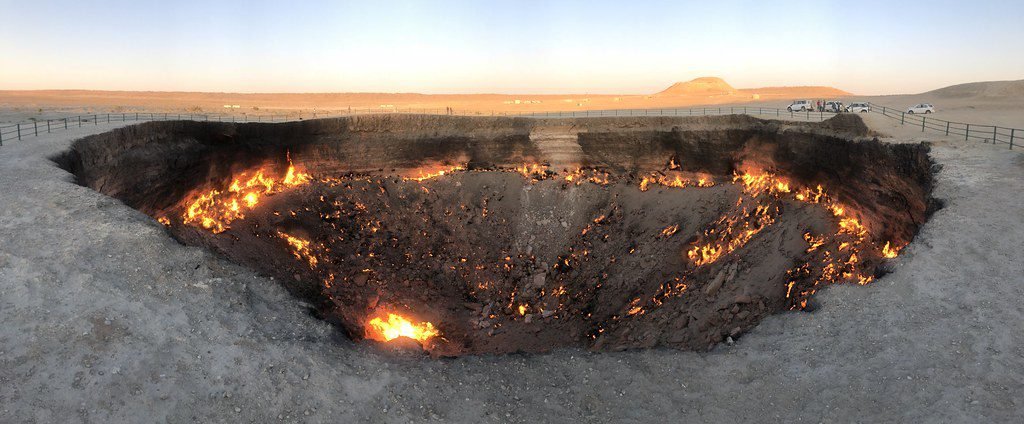 Panoramic view of the Darvaza Gas Crater, also known as the Door to Hell, located in Turkmenistan, showcasing the fiery flames and rugged terrain of the crater at sunset.