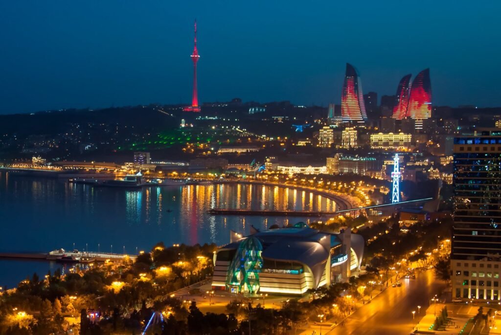 Night view of Baku, Azerbaijan, showcasing the illuminated Flame Towers, the TV tower, and the waterfront promenade along the Caspian Sea, with vibrant city lights reflecting on the water.