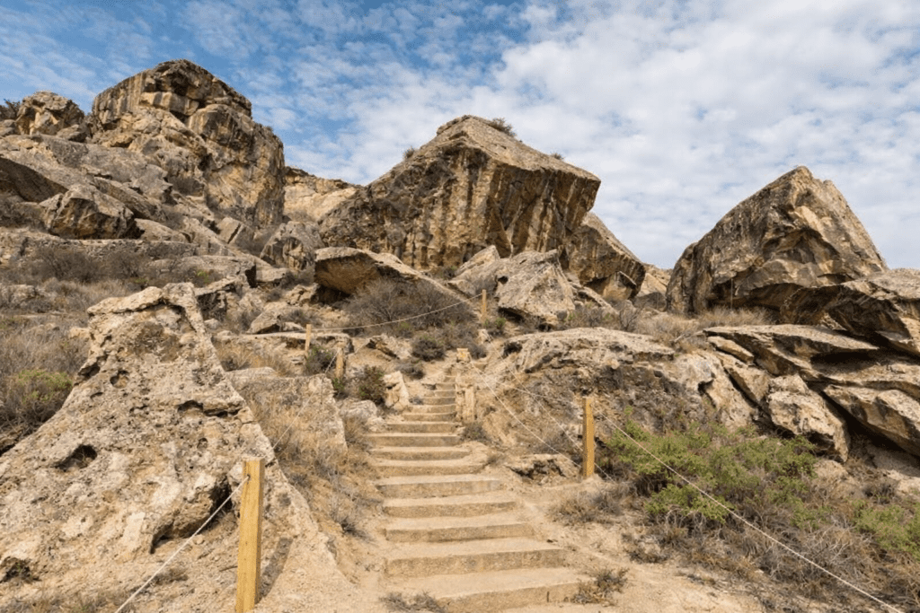 Rocky landscape with a winding stone staircase leading through boulders and sparse vegetation under a partly cloudy sky, ideal for hiking and outdoor exploration.