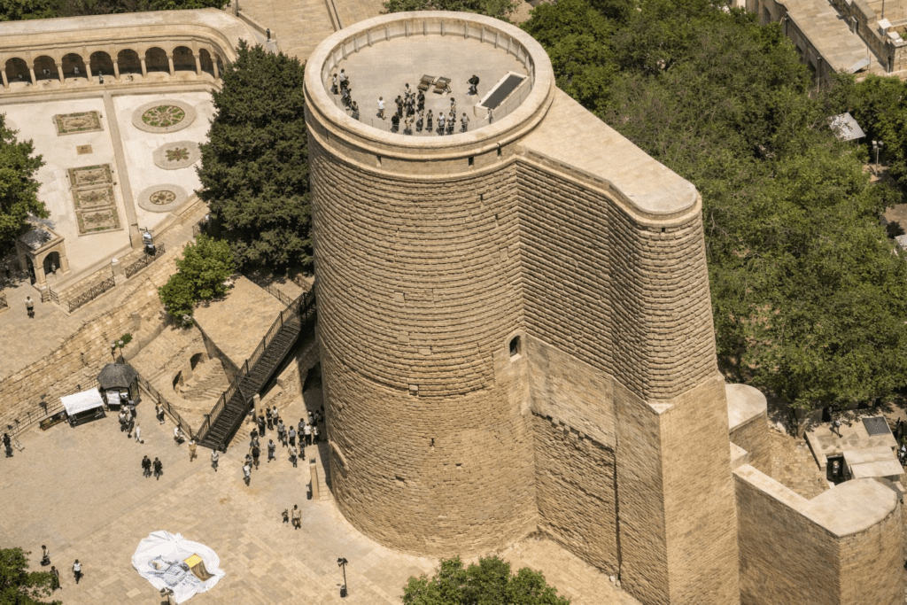 Aerial view of the Maiden Tower in Baku, Azerbaijan, showcasing its ancient stone architecture surrounded by greenery and visitors exploring the area.