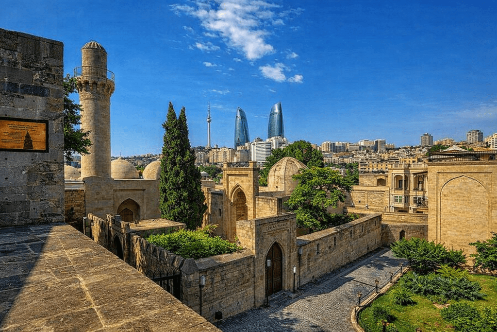 Baku's Old City featuring historical architecture, including a stone minaret and domed structures, with the modern Flame Towers skyline in the background under a clear blue sky.