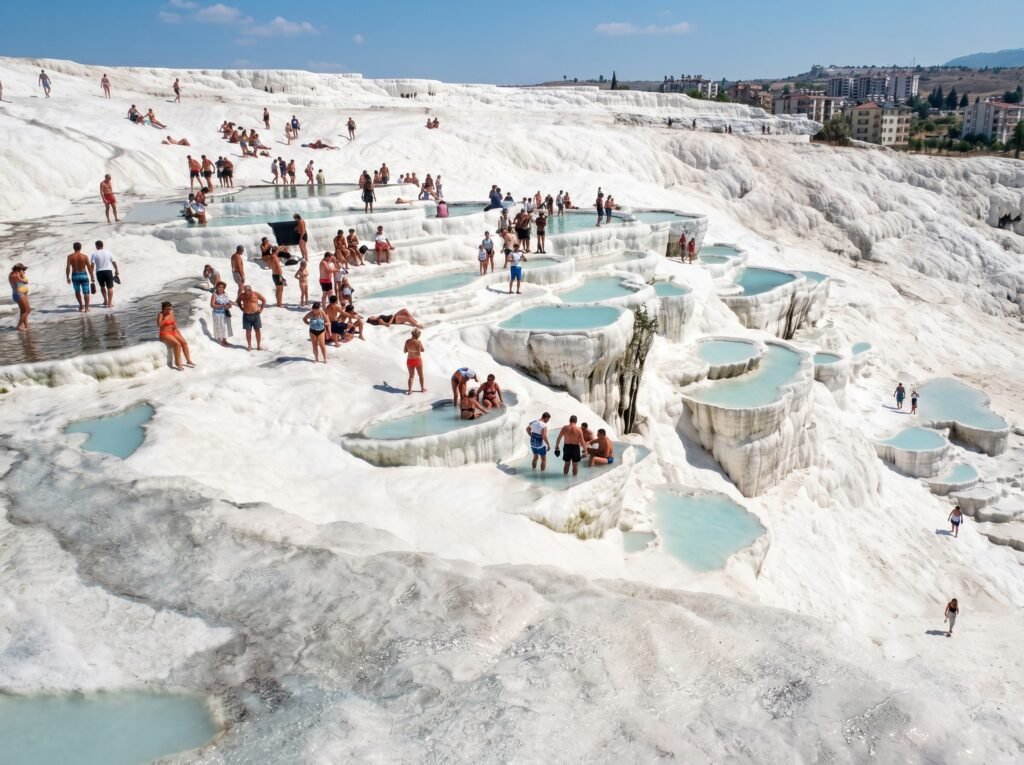 Tourists enjoying the thermal pools at Pamukkale, Turkey, surrounded by stunning white travertine terraces and clear blue waters on a sunny day.