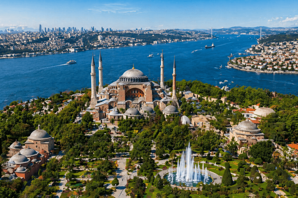 Aerial view of Hagia Sophia in Istanbul, showcasing its iconic dome and minarets surrounded by lush gardens and a fountain, with the Bosphorus River and city skyline in the background.