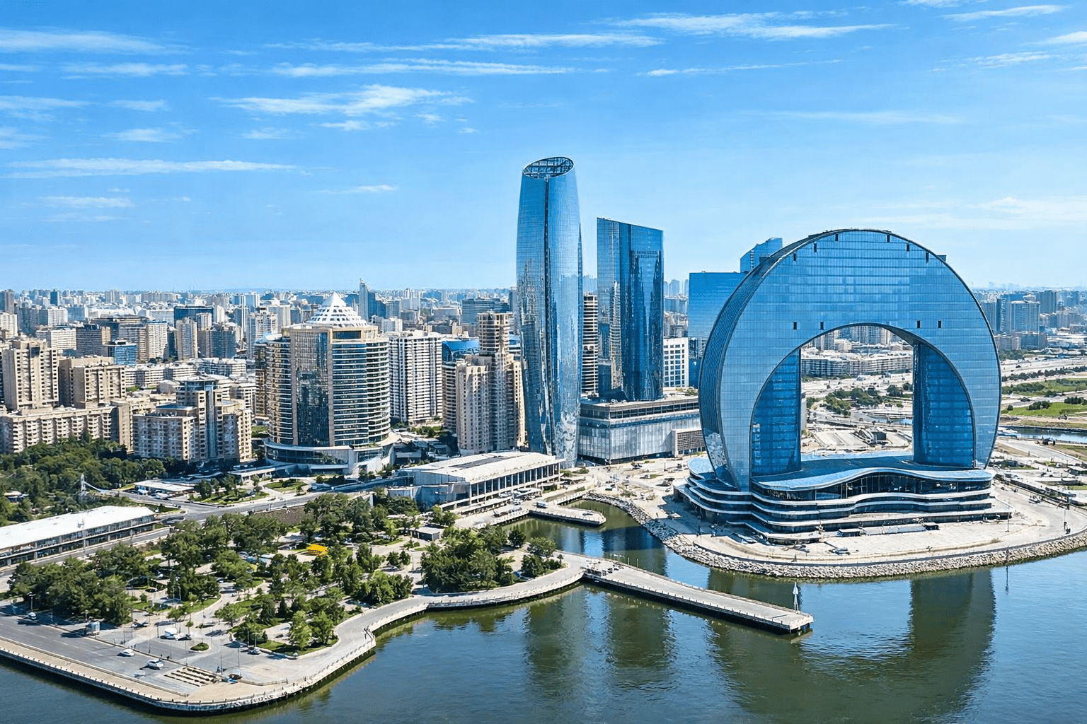Aerial view of modern skyscrapers in a vibrant cityscape featuring the unique architectural design of the large circular building by the river, surrounded by green parks and urban development under a clear blue sky.