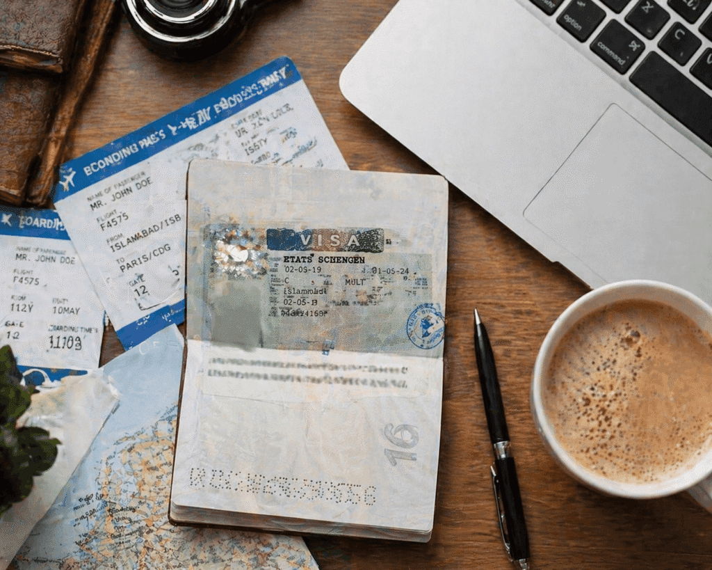 Close-up of a traveler's passport featuring a Schengen visa, surrounded by flight tickets, a map, a laptop, and a coffee cup, symbolizing travel planning and international journeys.