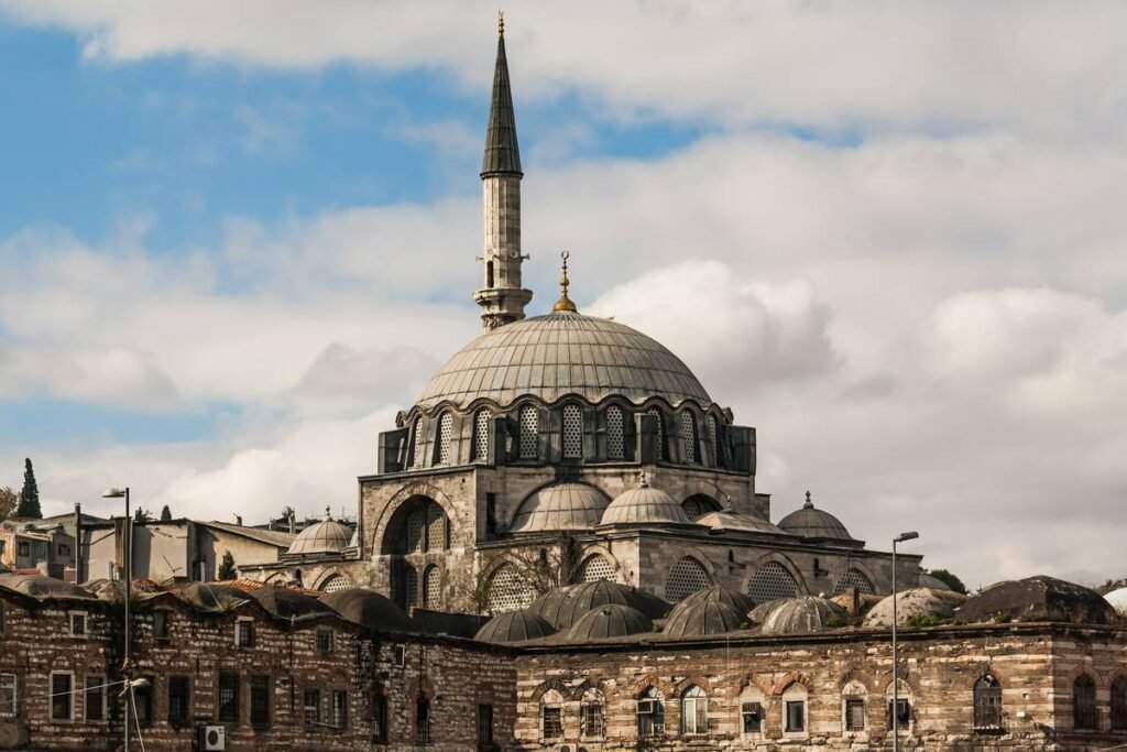 Historic mosque with a large dome and minaret, surrounded by traditional architecture and cloudy sky, showcasing the rich cultural heritage of the region.