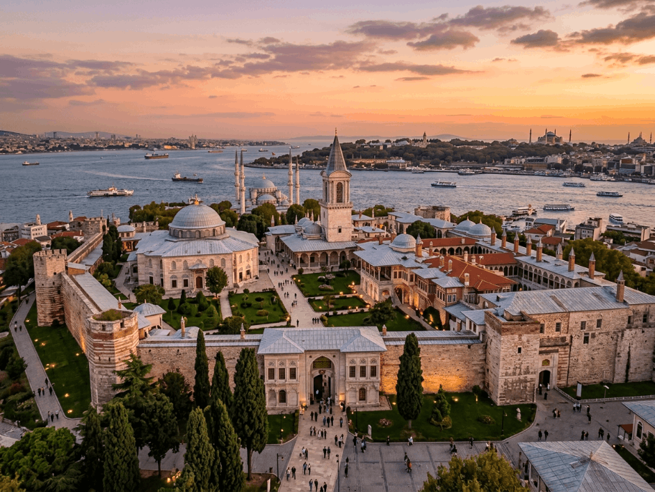 Aerial view of Topkapi Palace in Istanbul at sunset, showcasing its historic architecture, lush gardens, and the Bosphorus Strait in the background with boats sailing.