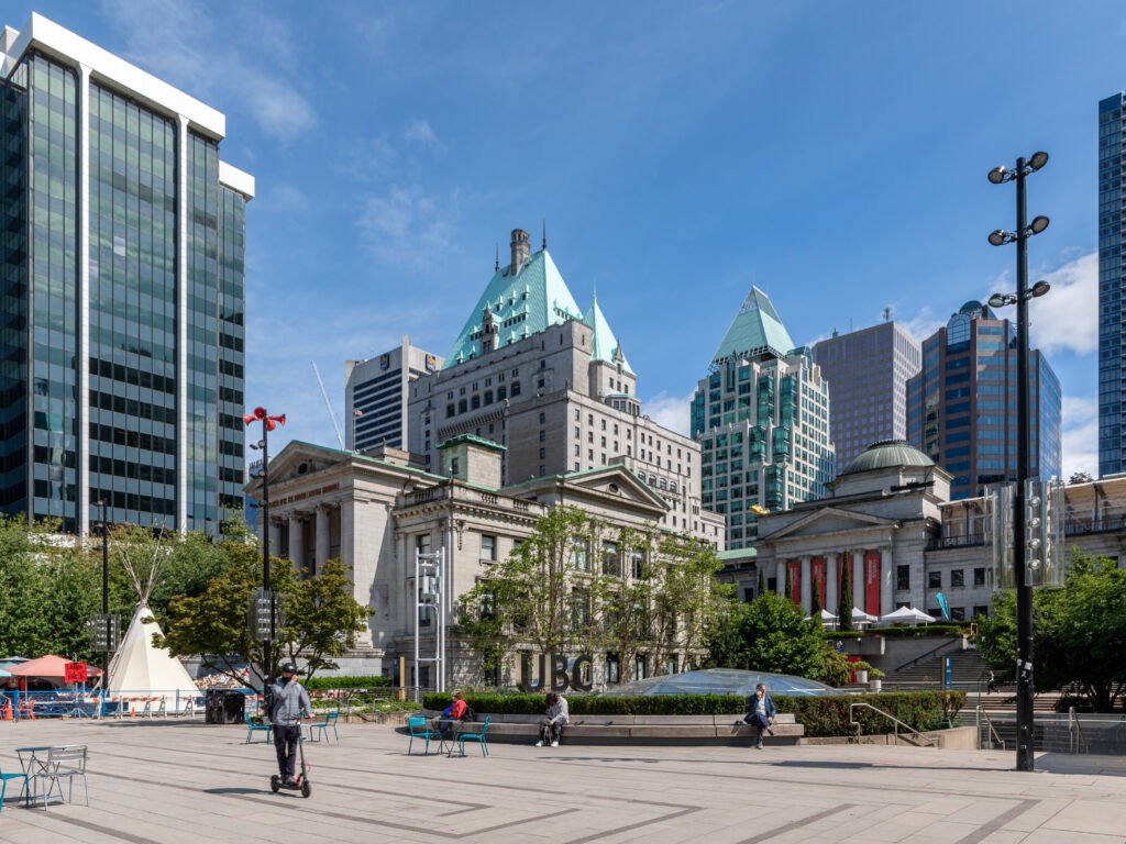 Cityscape of Vancouver showcasing a blend of historic and modern architecture, including the Vancouver Art Gallery, skyscrapers, and a public plaza with people enjoying the outdoor space.