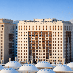 Exterior view of the Abraj Al Bait Clock Tower with decorative domes in the foreground, located in Mecca, Saudi Arabia, showcasing modern architectural design and traditional elements.