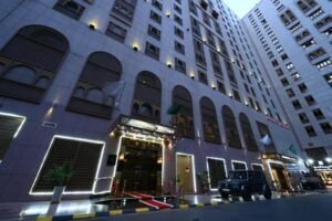 Exterior view of a luxury hotel featuring elegant architecture, illuminated entrance, and a black SUV parked at the front, showcasing a welcoming atmosphere in an urban setting.
