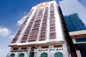 Facade of the Bakar Abdullah Hotel in Mecca, showcasing a blend of traditional architecture with modern design elements, featuring multiple windows and a prominent sign in Arabic and English.