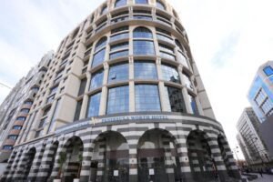 Exterior view of the Peninsula Worth Hotel featuring modern architectural design, large glass windows, and distinctive striped columns, located in a bustling urban setting. Ideal for travelers seeking luxury accommodations.