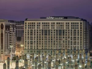 Modern hotel building in Medina, Saudi Arabia, featuring illuminated architectural details and surrounded by decorative columns at dusk.