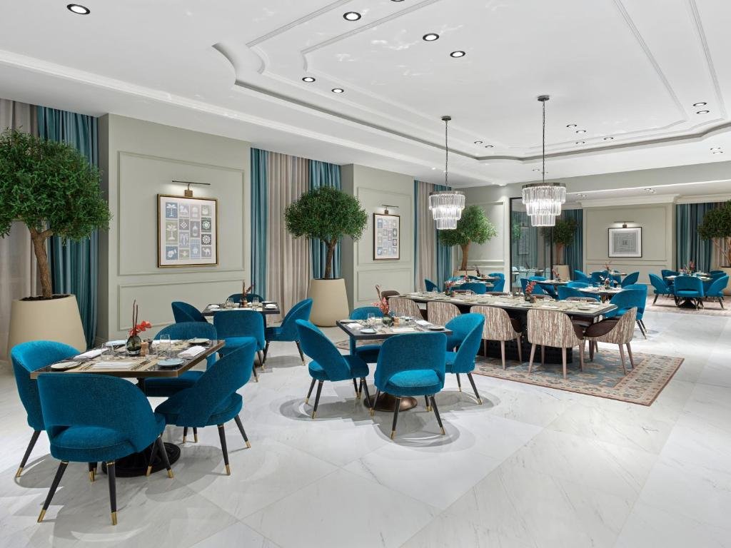 Elegant dining area at the Address Jabal Omar Makkah Hotel featuring blue chairs, decorative plants, and stylish lighting, creating a sophisticated atmosphere for guests.