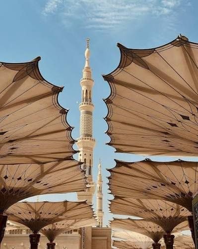 View of the iconic minaret surrounded by large, retractable umbrellas at Al-Masjid an-Nabawi in Medina, showcasing Islamic architecture under a clear blue sky.
