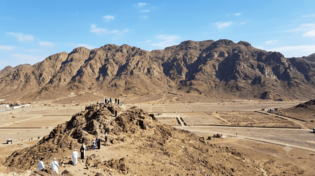 Panoramic view of rocky mountains in a desert landscape with visitors exploring the terrain, showcasing the natural beauty of the region.