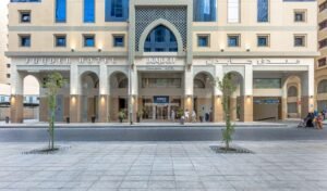 Front view of Jayden Hotel showcasing its modern architecture, entrance with arched columns, and signage in both English and Arabic, with pedestrians walking along the street.