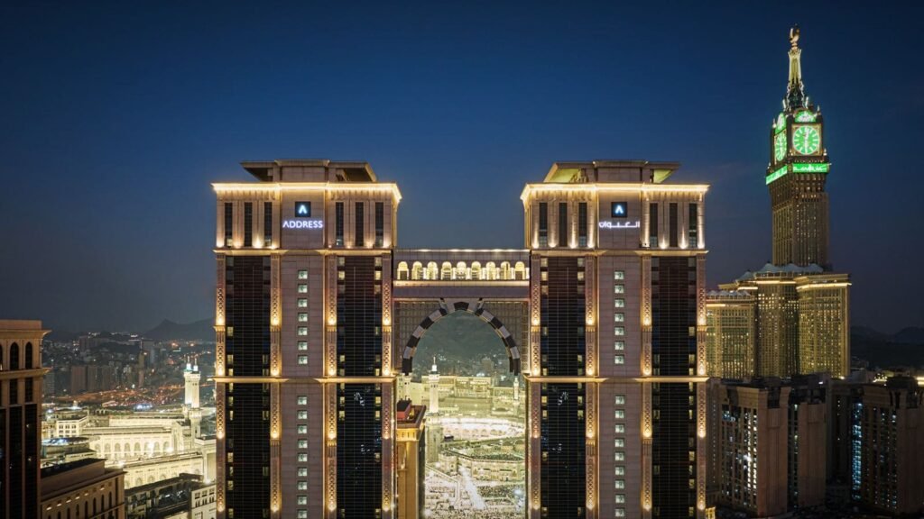 View of the illuminated Address Hotel towers at night, overlooking the Grand Mosque in Mecca, Saudi Arabia, with the iconic Abraj Al Bait clock tower in the background.