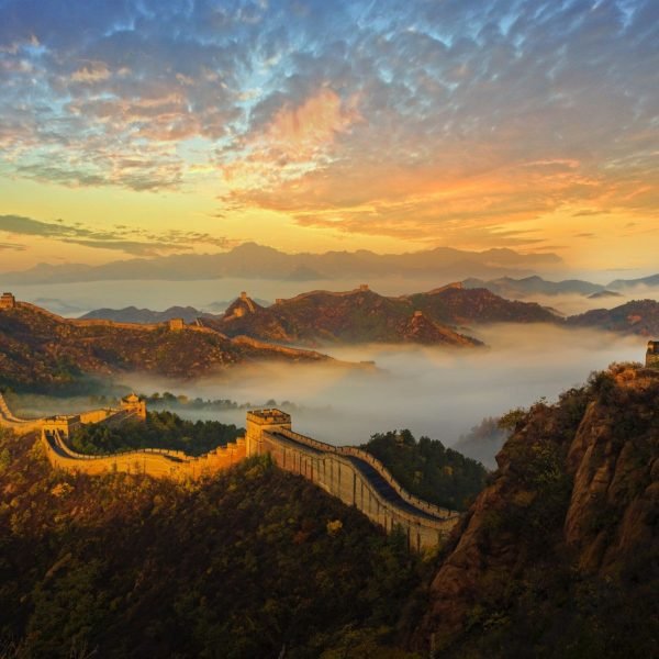Breathtaking view of the Great Wall of China at sunrise, surrounded by misty mountains and vibrant clouds, showcasing the ancient structure's winding path through a serene landscape.