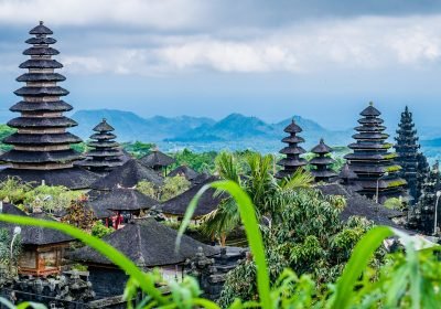 Scenic view of traditional Balinese temples surrounded by lush greenery and mountains under a cloudy sky in Bali, Indonesia.